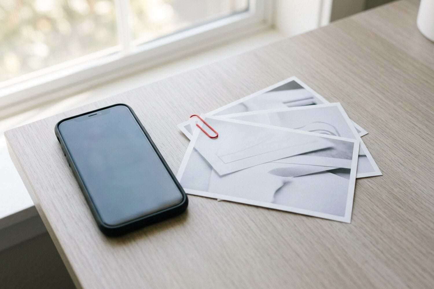 An iPhone on a desk next to three printed photos of documents held together by a red paper clip